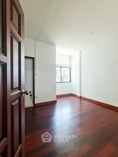 Spacious empty room with wooden flooring and large window, perfect for customization.