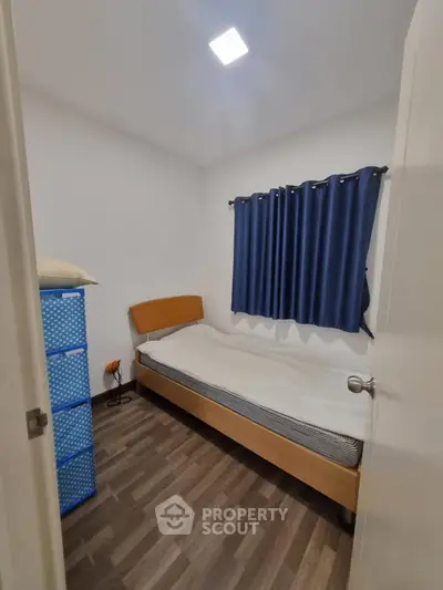 Cozy small bedroom with wooden flooring and blue curtains, perfect for a minimalist lifestyle.