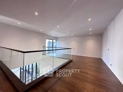 Spacious modern interior with sleek glass railing and hardwood floors, perfect for contemporary living.