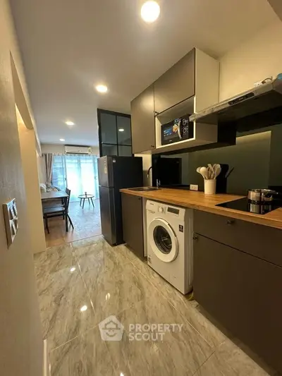 Modern kitchen with washing machine and sleek cabinetry in open layout apartment.