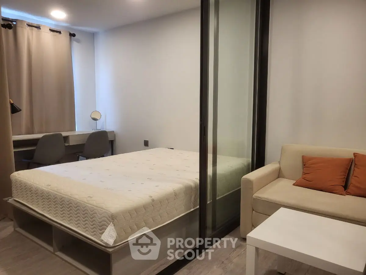 Modern studio apartment with cozy bed, sofa, and study area, featuring sleek glass partition.