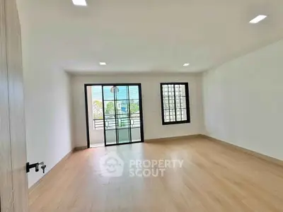 Spacious empty room with wooden flooring and balcony access, ideal for customization.