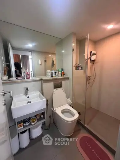 Modern bathroom with glass shower, sleek sink, and toilet in a contemporary apartment.