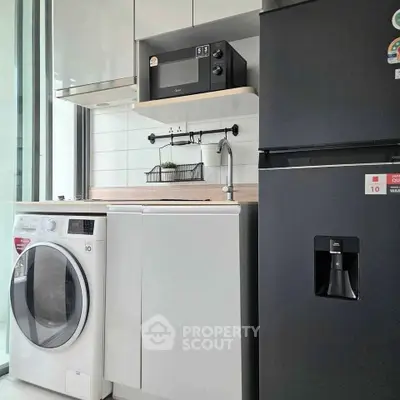 Modern kitchen with sleek appliances including fridge, washing machine, and microwave in a compact layout.