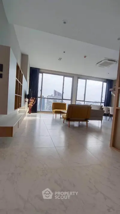 Spacious modern living room with large windows and city view, featuring stylish furniture and elegant flooring.