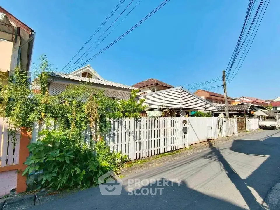 Charming suburban house with white picket fence and lush greenery under clear blue sky.