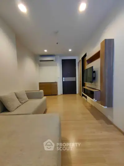 Modern living room with sleek furniture and wooden flooring, featuring a wall-mounted TV and ambient lighting.