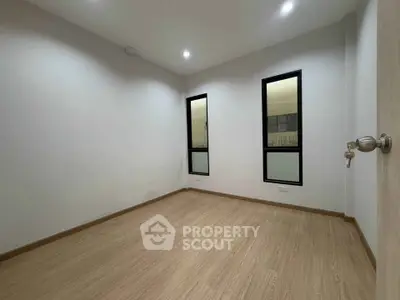 Spacious empty room with wooden flooring and large windows, perfect for customization.