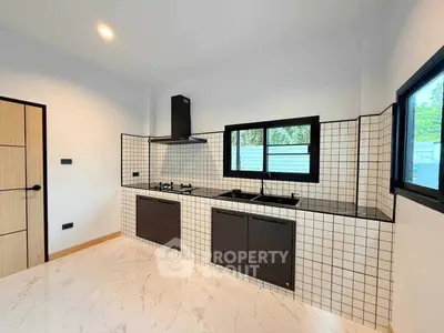 Modern kitchen with sleek black cabinets and gas stove in a bright, tiled space.