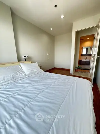 Spacious bedroom with cozy bed and ensuite bathroom in modern apartment.