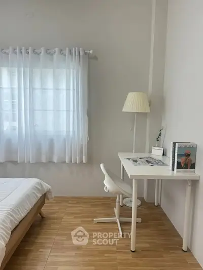 Cozy bedroom with study area, featuring a white desk and chair, wooden flooring, and natural light.