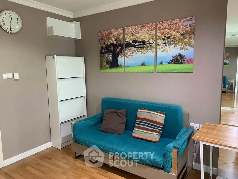 Cozy living room with teal sofa, wall art, and wooden flooring, perfect for relaxation.