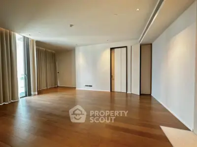 Spacious empty living room with wooden flooring and large windows.