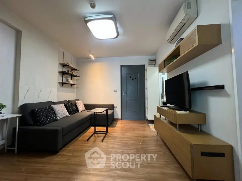 Modern living room with sleek furniture and wooden flooring, featuring a wall-mounted TV and stylish shelving.