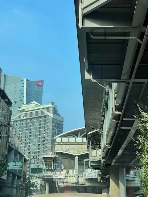 Urban cityscape with modern high-rise buildings and elevated train tracks under a clear blue sky.