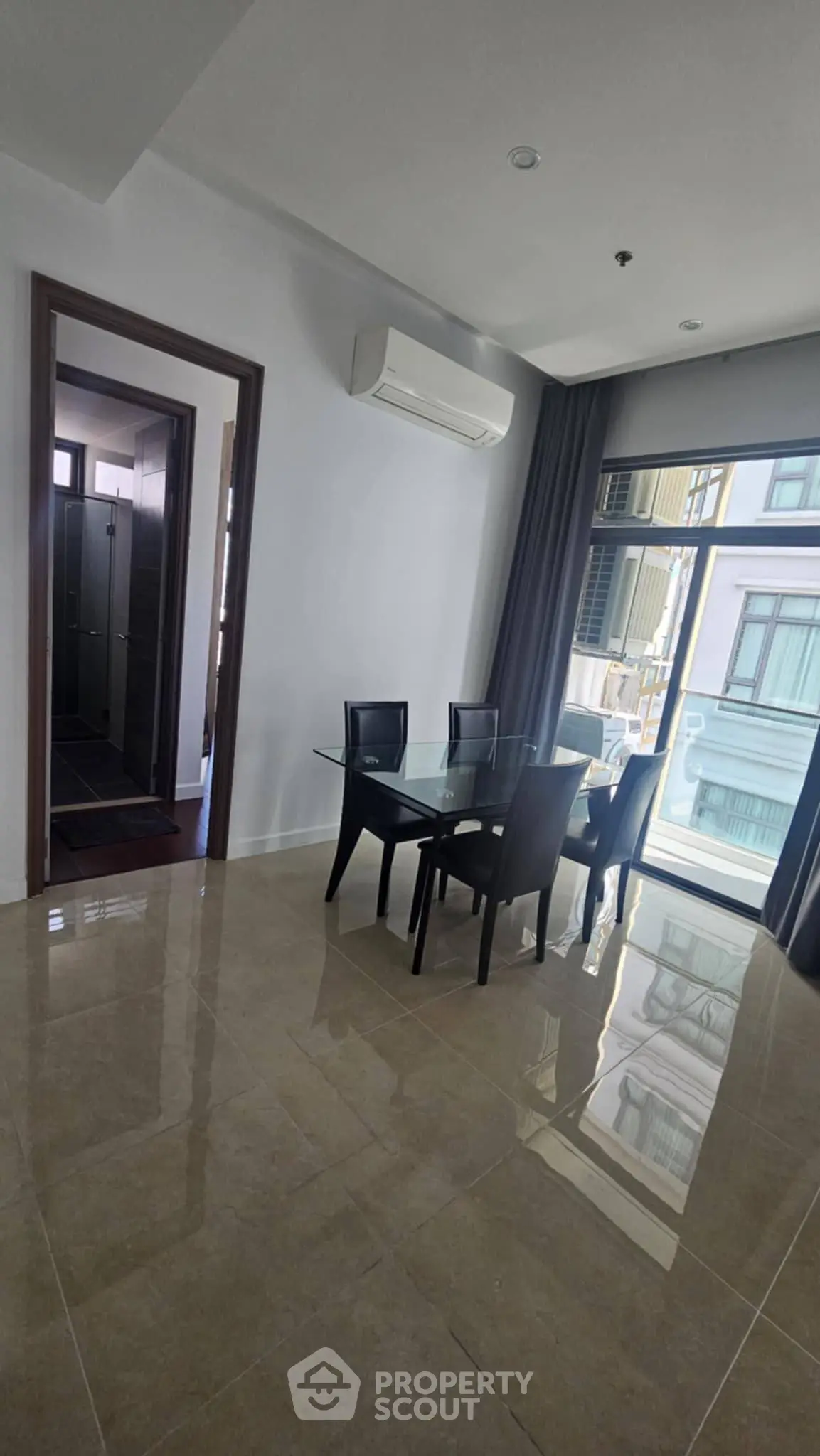 Modern dining area with glass table and chairs, featuring large windows and sleek tile flooring.