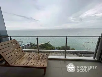 Stunning ocean view from a modern balcony with wooden lounge chair.