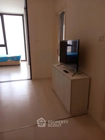 Modern apartment interior with TV cabinet and view into bedroom, featuring large windows and natural light.