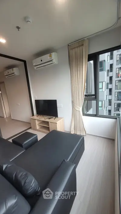 Modern living room with sleek black sofa, wall-mounted TV, and large window offering city views.