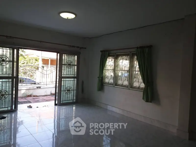 Spacious living room with large windows and tiled floor, offering ample natural light.