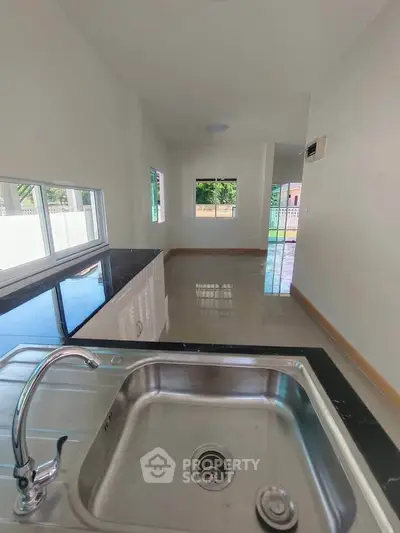 Modern kitchen with sleek sink and open layout, featuring large windows and glossy tiles.