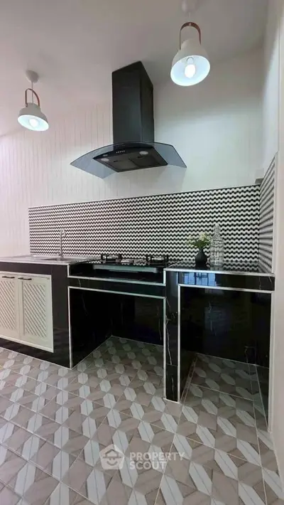 Modern kitchen with sleek black countertops and stylish backsplash, featuring a gas stove and elegant lighting.