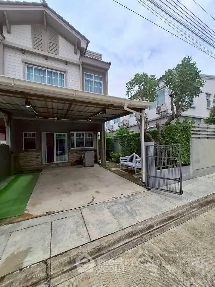 Charming two-story house with covered parking and lush greenery in a peaceful neighborhood.