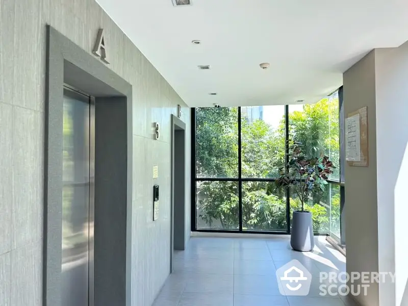 Modern building elevator lobby with large windows and lush greenery view.