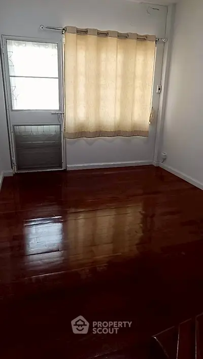 Spacious room with polished wooden floors and natural light from window.