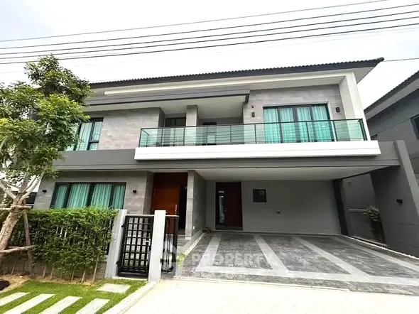 Modern two-story house with spacious driveway and balcony, featuring sleek architectural design and lush greenery.