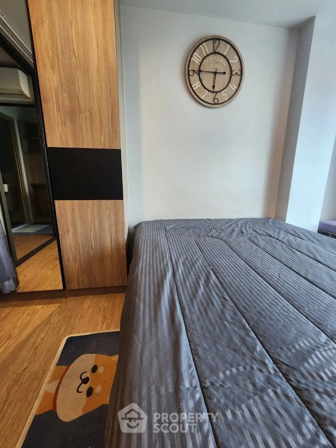 Cozy bedroom with stylish clock and wooden wardrobe, featuring a playful rug for a charming touch.