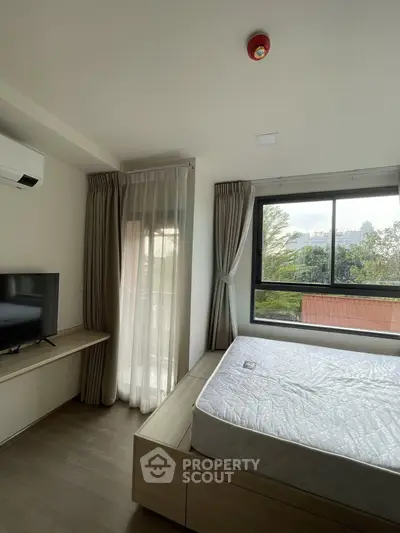 Modern bedroom with large window and natural light, featuring a bed and TV, ideal for comfortable living.