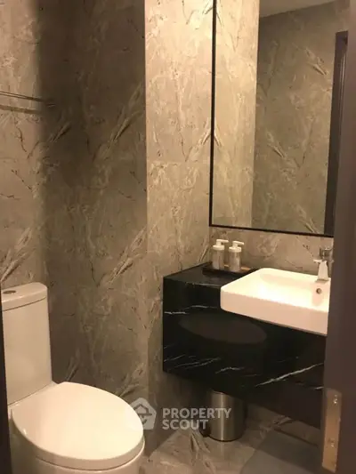 Modern bathroom with sleek design and marble walls, featuring a contemporary sink and toilet.