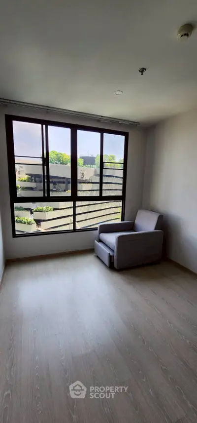 Spacious room with large window and modern armchair, offering a serene view of the outdoors.