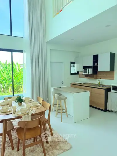 Modern open-layout kitchen and dining area with high ceilings and large windows overlooking greenery.