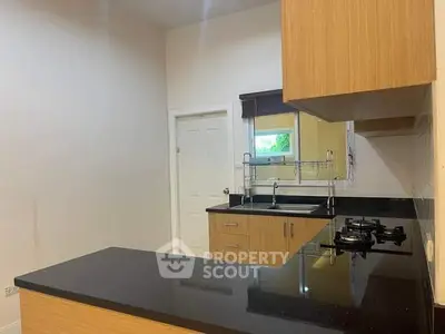 Modern kitchen with sleek black countertops and wooden cabinets, featuring a gas stove and ample storage space.