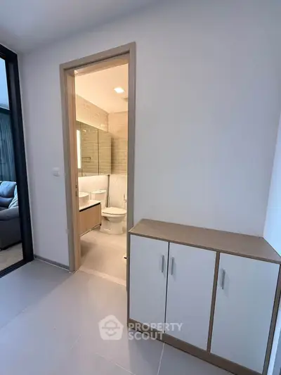 Modern apartment hallway leading to a stylish bathroom with sleek fixtures and neutral tones.