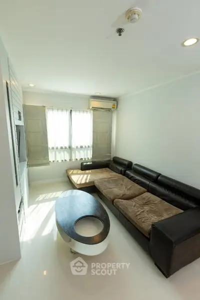 Modern living room with sleek black leather sofa and stylish coffee table, featuring natural light from large windows.