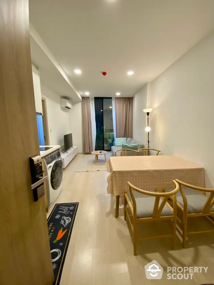 Modern living room with open layout and stylish furniture, featuring a washing machine and large window view.