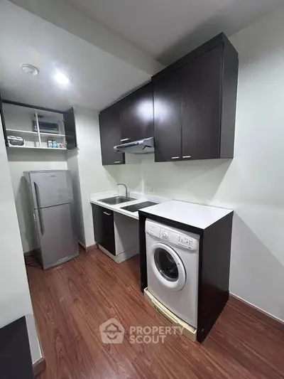 Modern kitchen with sleek cabinets, washing machine, and fridge in compact layout.
