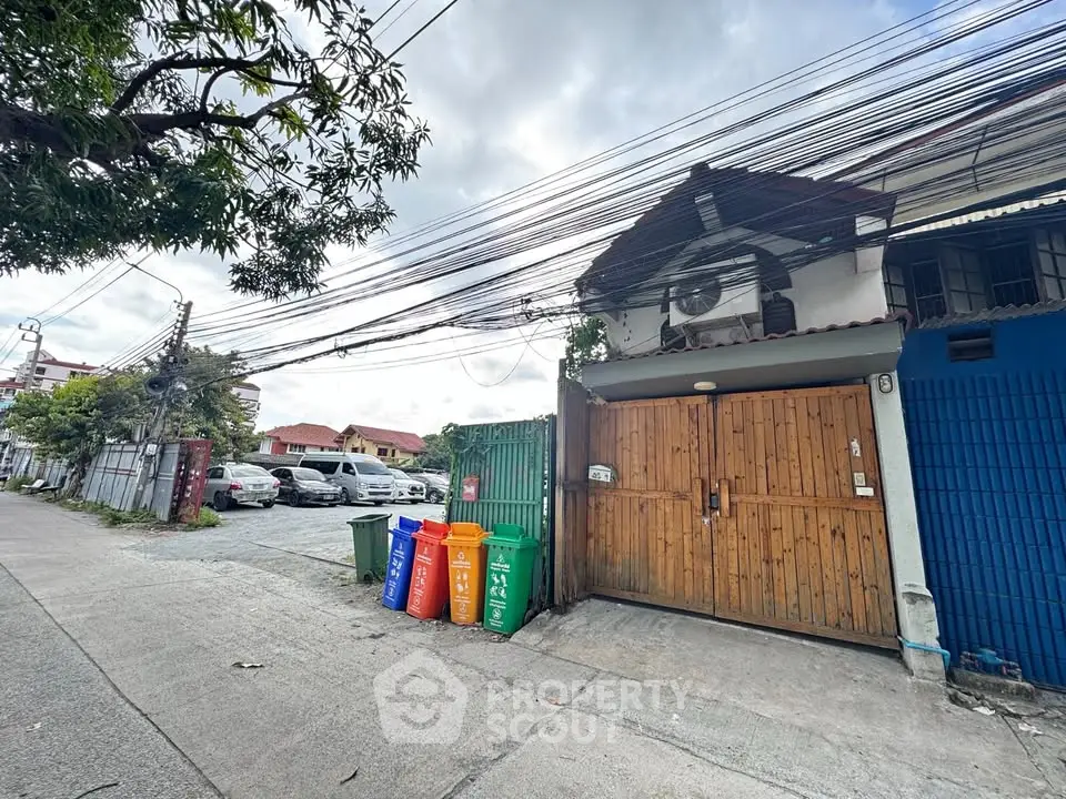 Charming residential property with wooden gate and colorful recycling bins, ample parking space nearby.