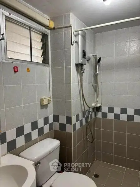 Compact bathroom with shower and toilet in modern tiled design.