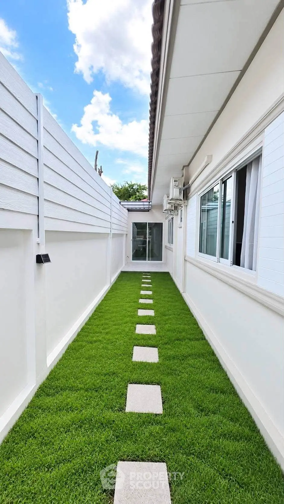 Charming narrow garden path with lush green grass and stepping stones beside a modern house exterior.