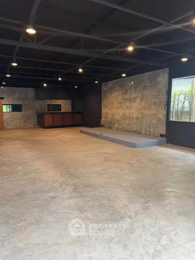 Spacious industrial-style interior with concrete floors and exposed ceiling beams, ideal for creative workspace.