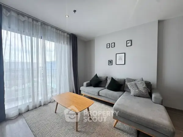 Modern living room with stylish gray sofa and wooden coffee table, featuring floor-to-ceiling windows.
