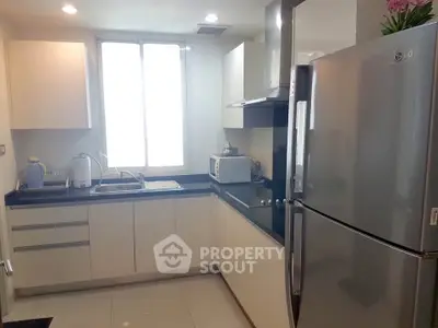 Modern kitchen with sleek cabinets, stainless steel fridge, and ample natural light.