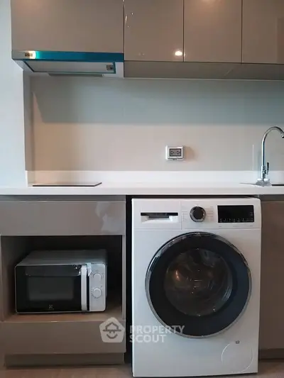 Modern kitchen with washing machine and microwave, sleek cabinetry, and minimalist design.