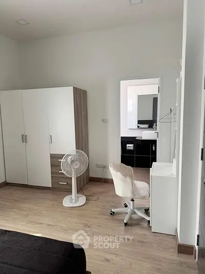 Modern bedroom with sleek furniture and a fan, featuring a view into a stylish bathroom.