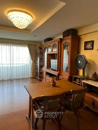 Elegant living room with wooden furniture and chandelier, featuring a cozy dining area and large window.