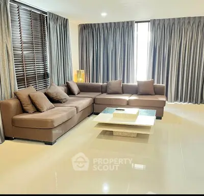 Spacious living room with modern brown sectional sofa and elegant floor-to-ceiling curtains.